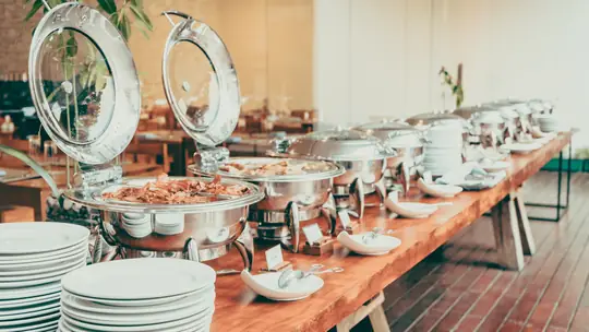 Mesa de buffet com réchauds e pilhas de pratos