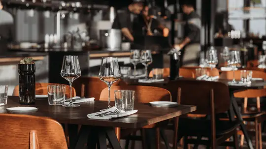 Salão de restaurante com mesas montadas, taças e talheres